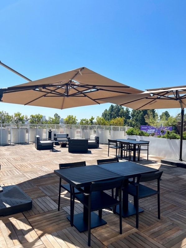 Terrassa exterior amb paviment de fusta, mobles negres i grans ombrel·les beix.