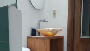 A bathroom with a white toilet, a wooden vanity with a glass bowl sink, a mirror, and a wooden door. - Arles ByB Cafe (San Cristóbal de las Casas)