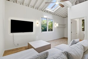 A spacious room with a large flat-screen TV mounted on the wall, a wooden coffee table, a sofa, and a skylight above. - Atherton Garden ADU in Silicon Valley (Atherton)