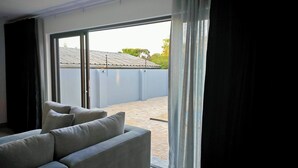 A modern living room with a sofa, a sliding glass door leading to an outdoor area. - Room-courtyard Room With Shared Bathroom (Cape Town)