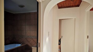 A bathroom with a bathtub, a shower area, and a tiled wall. - Room-courtyard Room With Shared Bathroom (Cape Town)