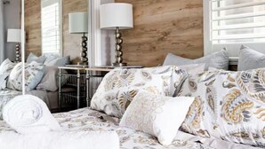 Une chambre à coucher avec un grand lit, un miroir, une table de chevet avec une lampe et une fenêtre avec des stores.