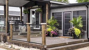Un espace extérieur abrité doté d’une terrasse en bois, de plantes en pot et d’un bâtiment avec de grandes fenêtres.