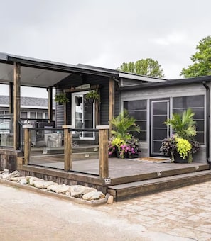 A covered outdoor area with a wooden deck, potted plants, and a building with large windows.