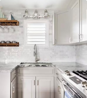 A kitchen with white cabinets, a window with blinds, a stainless steel sink, and a gas stove.