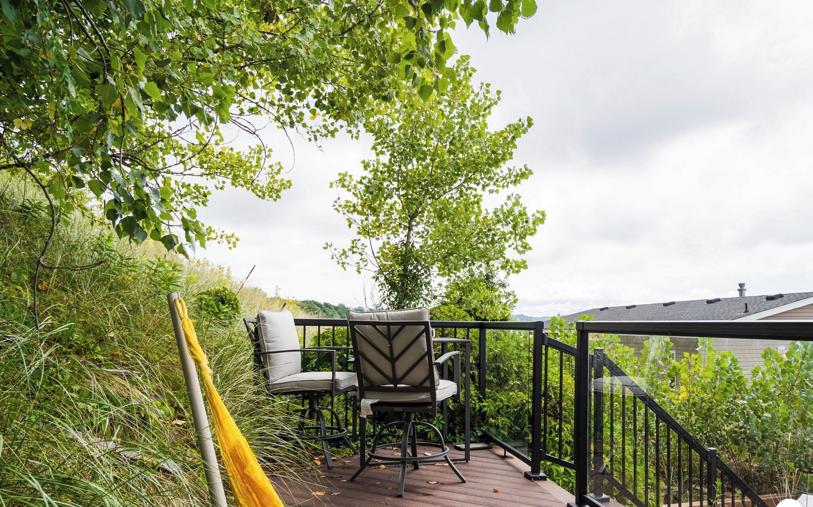 A patio with a chair and table, surrounded by greenery and a railing.