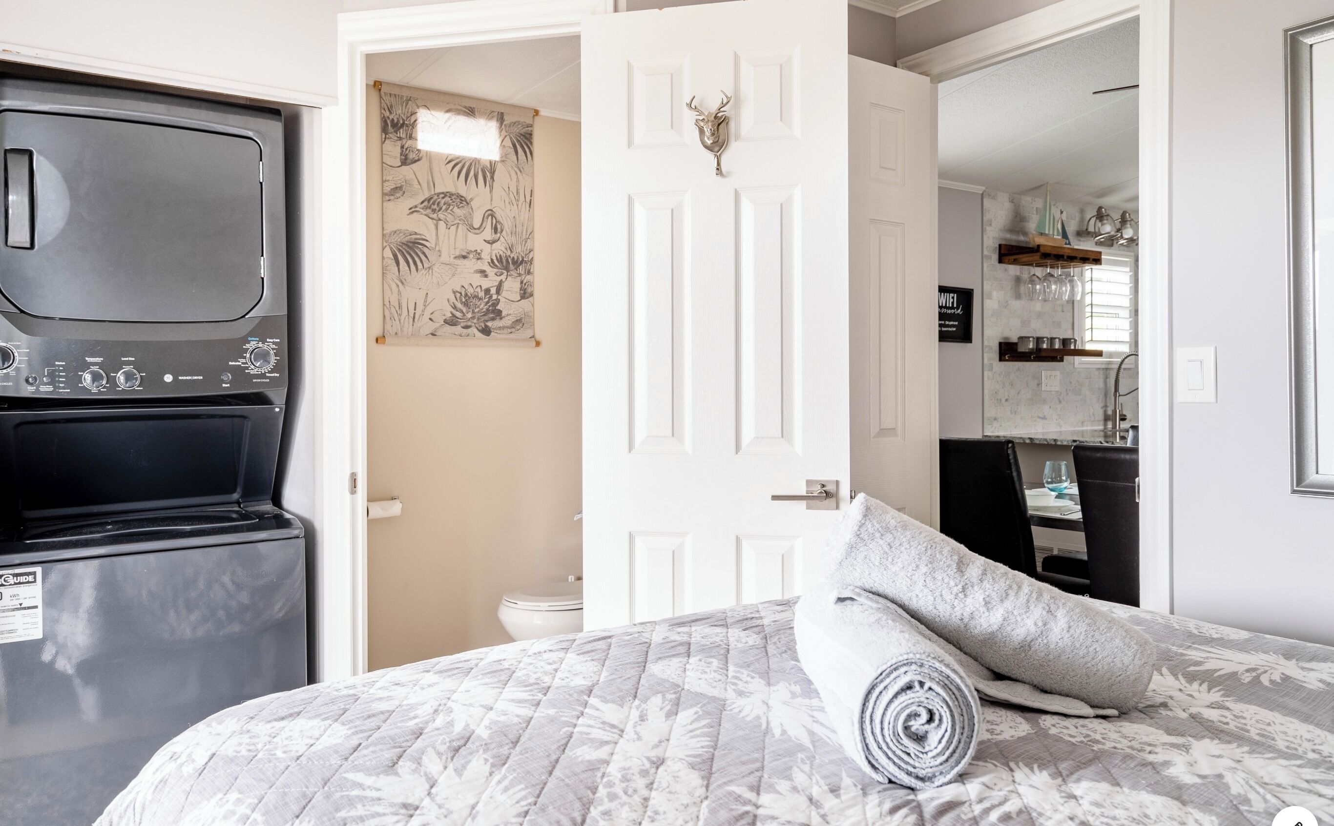 Quarto com cama, porta branca, cozinha compacta e banheiro.