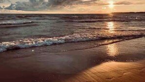 Une scène de plage avec des vagues, un coucher de soleil et un ciel nuageux.