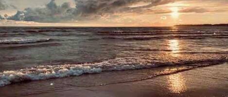 Une scène de plage avec des vagues, un coucher de soleil et un ciel nuageux.
