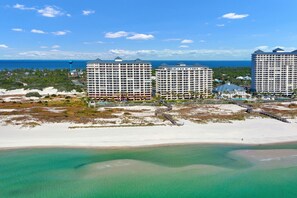 Un hotel frente a la playa con varios edificios altos, una playa de arena y aguas azules cristalinas.