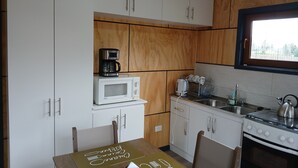 A compact kitchen with white cabinets, a microwave, a coffee maker, a kettle, and a stove.