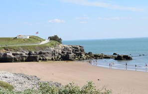 Ein Küstenstrand mit felsigen Klippen, eine Flagge auf einem Hügel und freie Sicht auf das Meer.