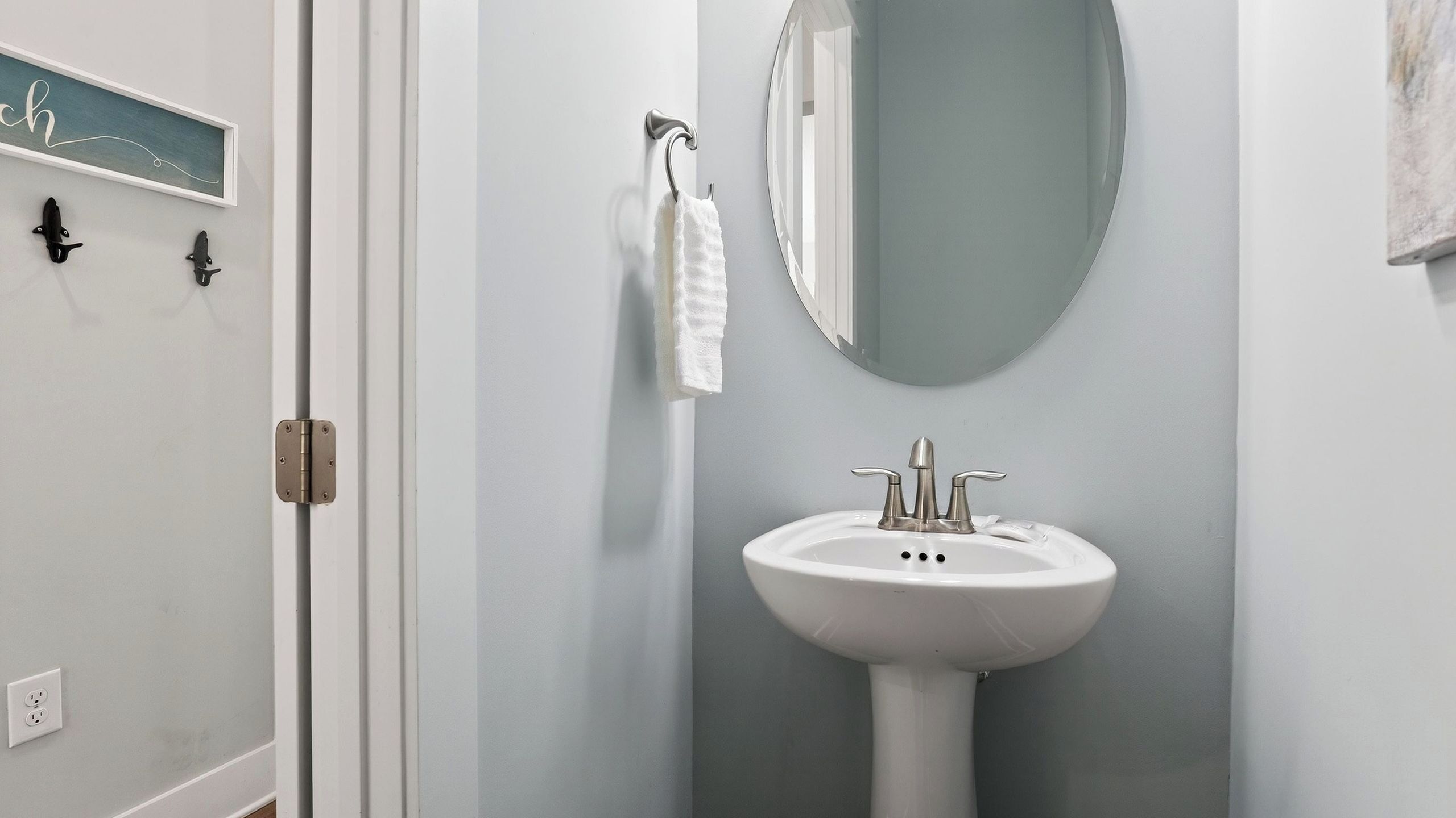 A bathroom with a white sink, a mirror, and a towel hanging on a hook.