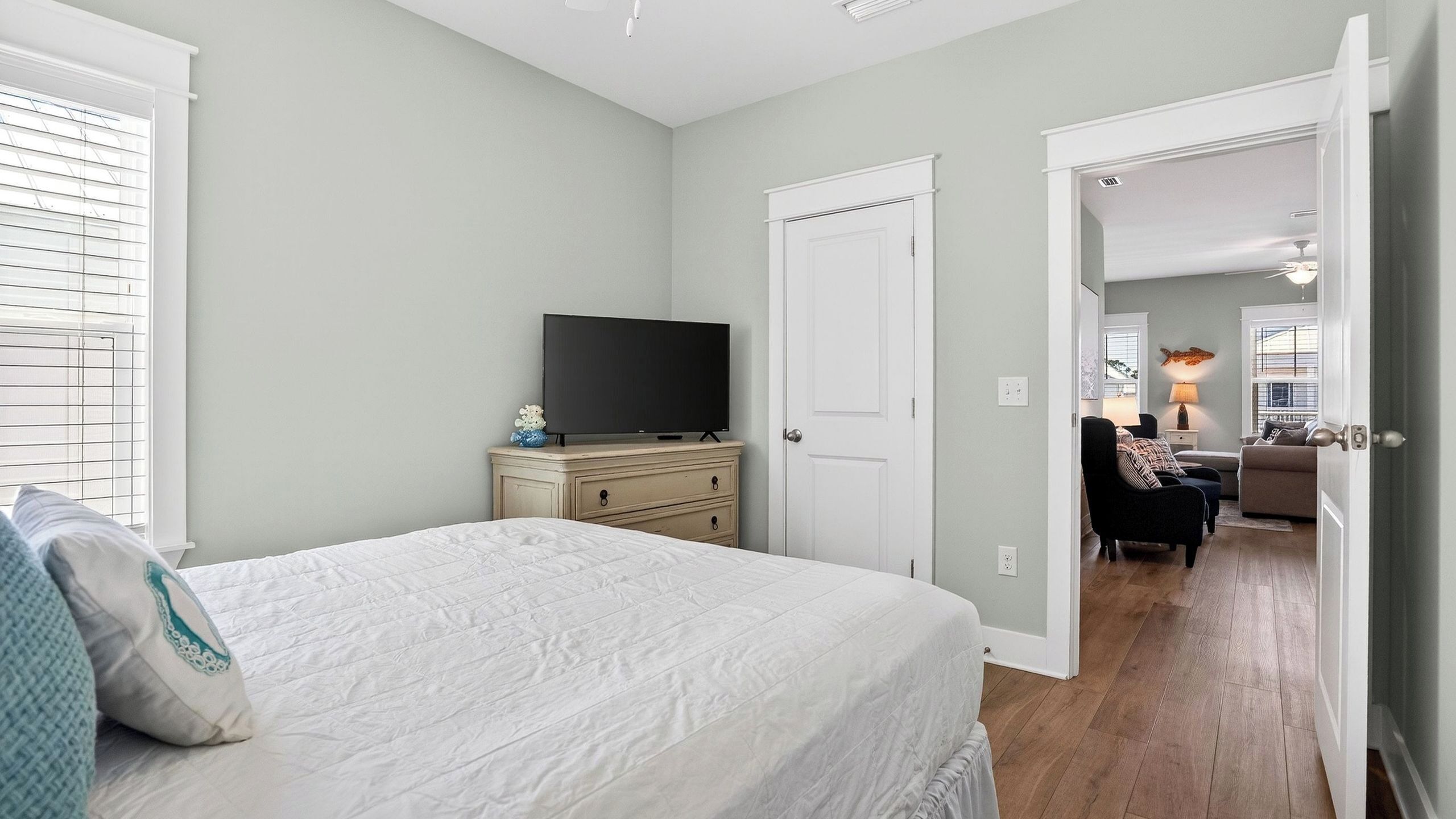 Ein Schlafzimmer mit Bett, Kommode, Fernseher und einer Tür zu einem anderen Raum.