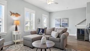 A living room with a grey sofa, a coffee table, a lamp, and artwork on the walls. - Southern Dreams on 30A by Avantstay Pool + Outdoor Lounge + Golf Cart Access Minutes to the Beach (Santa Rosa Beach)