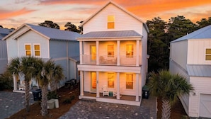 A two-story building with a balcony, surrounded by palm trees and other vegetation. - Southern Dreams on 30A by Avantstay Pool + Outdoor Lounge + Golf Cart Access Minutes to the Beach (Santa Rosa Beach)