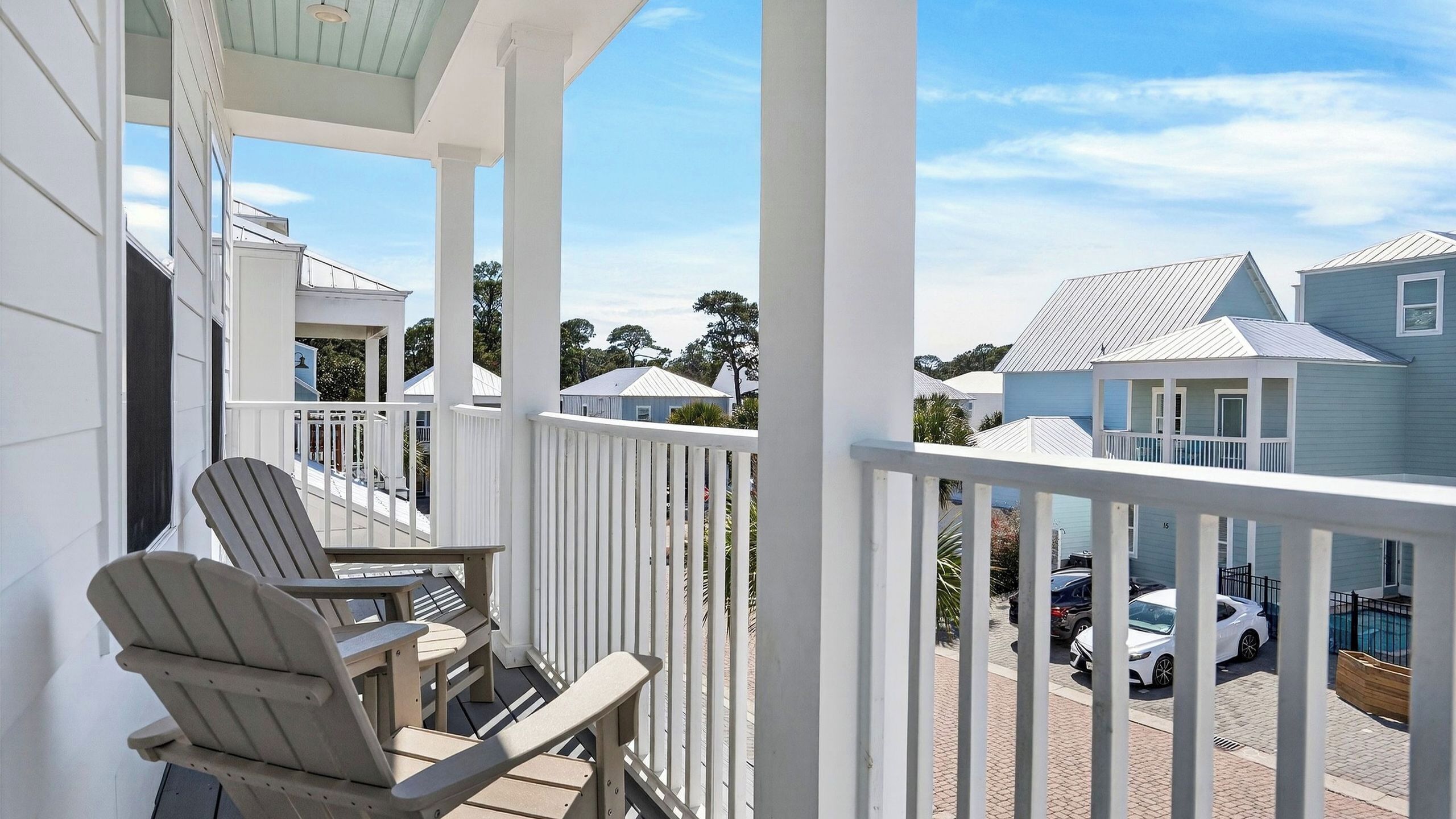 Eine überdachte Veranda mit zwei Adirondack-Stühlen, Blick auf benachbarte Häuser und eine gepflasterte Auffahrt mit parkenden Autos.
