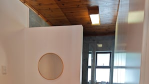 Ein Zimmer mit einem Holztisch, einem Stuhl, einem runden Spiegel und Blick in eine Küchenzeile.