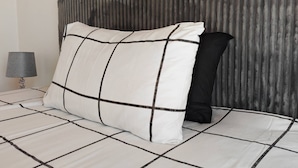 Ein Bett mit kariertem Überwurf, ein Kissen mit Gittermuster und ein Kopfteil mit vertikalen Rillen.