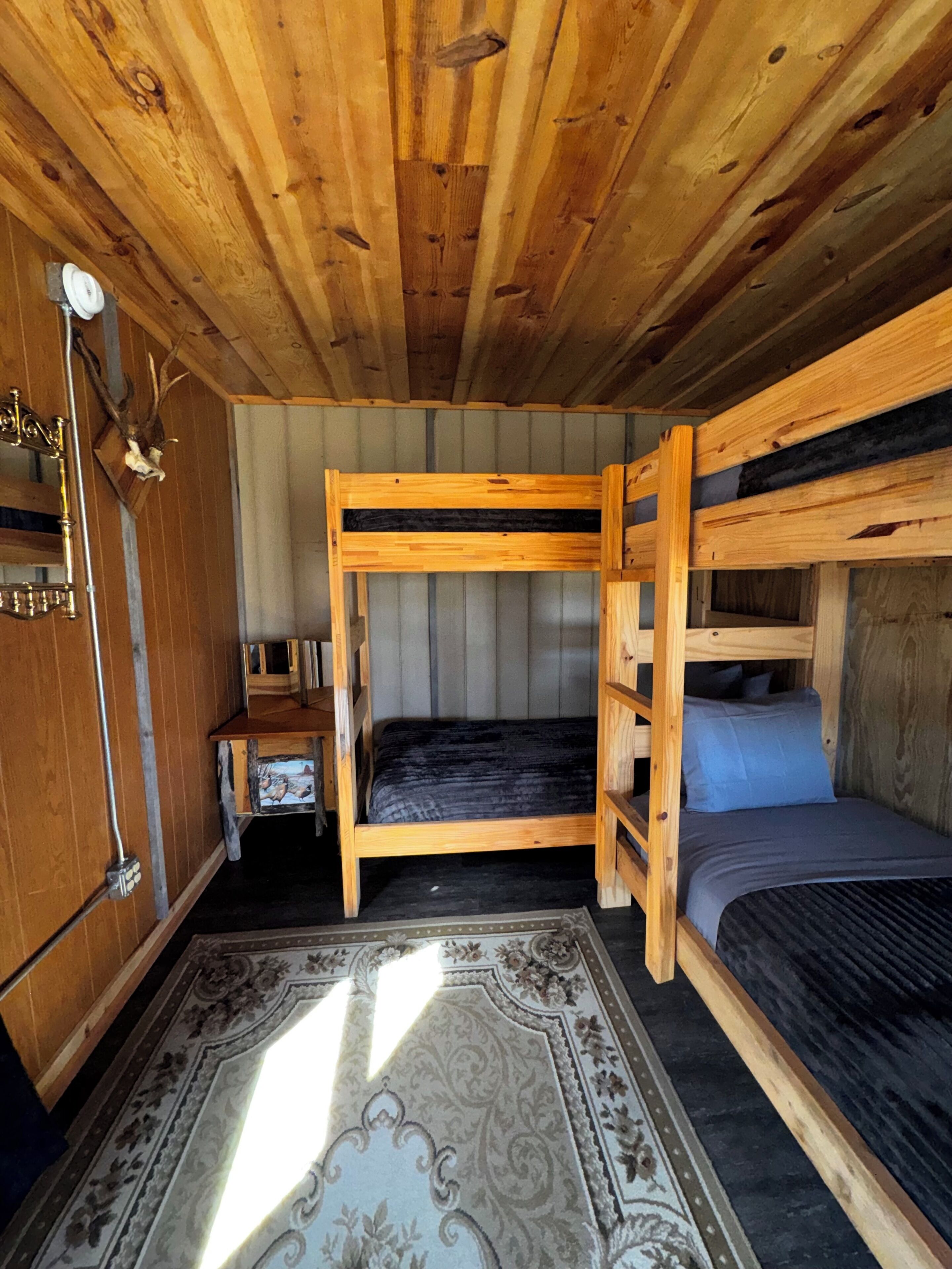 A wooden bunk bed room with a small table and a decorative rug.