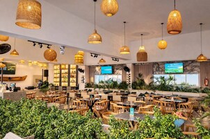 Un restaurante amplio con iluminación colgante de mimbre, varias zonas de estar y una pantalla de televisión.