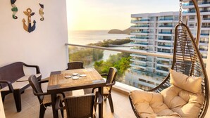 A balcony with a table, chairs, a hanging chair, and decorative wall art. - Ocean View and Direct Beach in Pozos Colorados (Santa Marta)