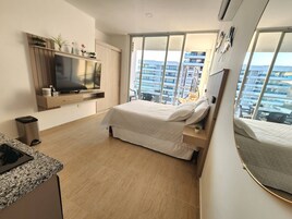Habitación de hotel moderna con una cama grande, televisor, escritorio pequeño y balcón con vista a la ciudad.