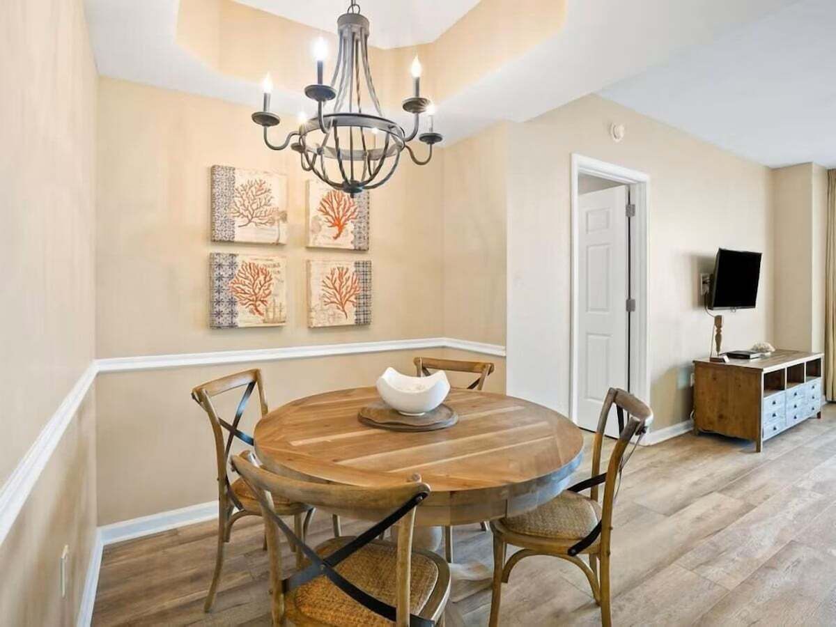 Un comedor con una mesa redonda de madera, cuatro sillas, una araña y decoración en la pared.