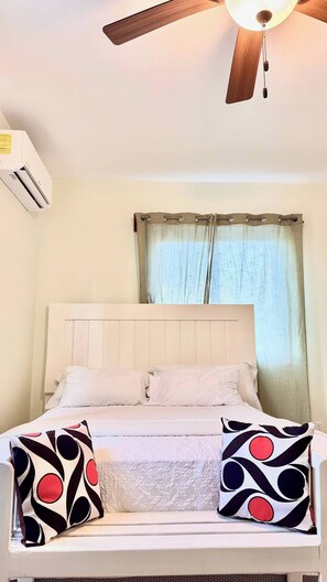 Ein Bett mit weißer Bettwäsche, einem Deckenventilator und einem fenster mit Vorhängen.