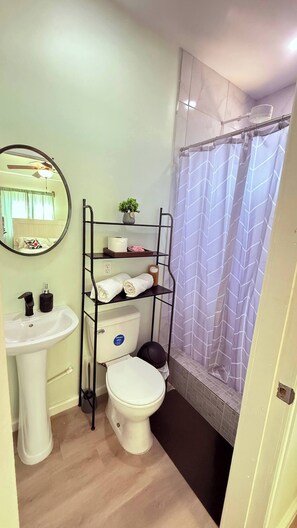 Ein kleines Badezimmer mit Toilette, Waschbecken und Duschbereich mit gemustertem Vorhang.