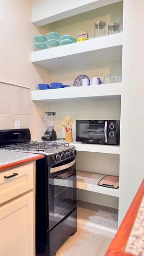 Eine Küche mit Gasherd, Backofen, Mikrowelle und Regalen mit Küchenutensilien.