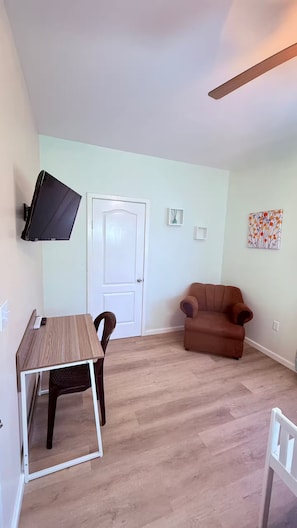 Ein Zimmer mit einem Holztisch, einem braunen Stuhl, einem braunen Sofa, einer weißen Tür und einem Wandfernseher.