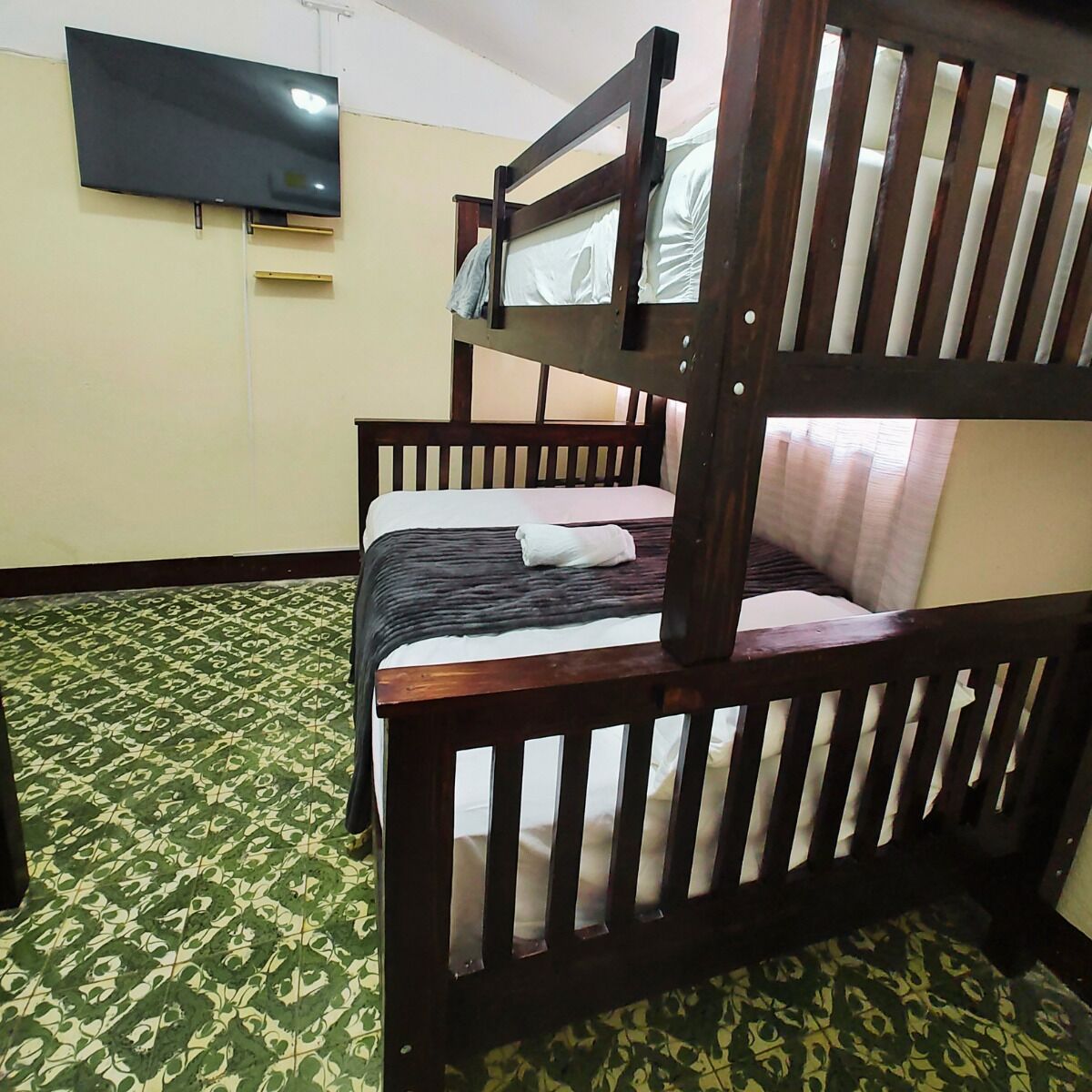 Habitación con literas, un televisor en la pared, alfombra estampada y una ventana con cortinas.