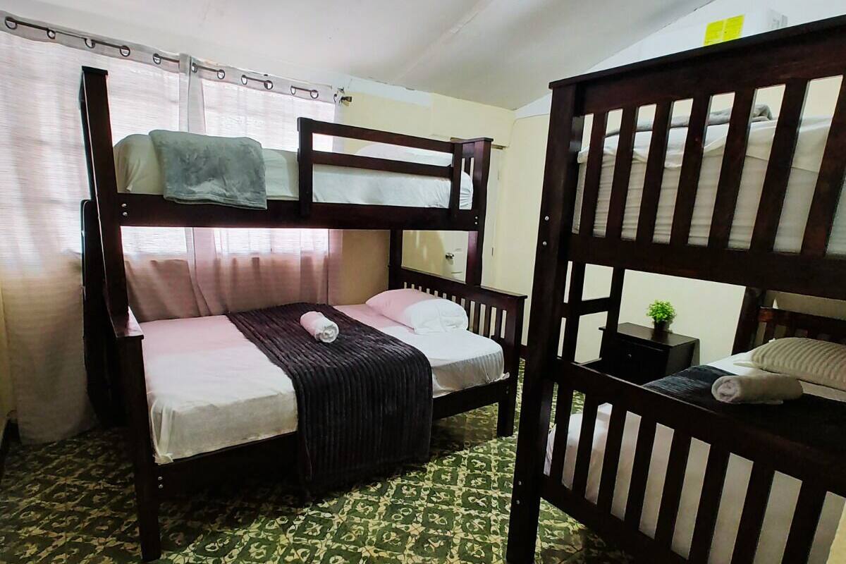 A bunk bed room with a patterned floor, a small table with a plant, and a window with curtains.