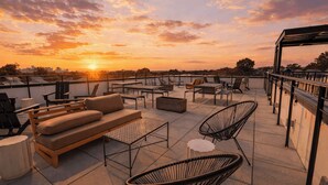 A rooftop terrace with a sofa, chairs, and a table, overlooking a sunset. - The Bloom House & Cosmic Cowgirl by Avantstay Sleeps 17 + 2 Units Gym + Rooftop + Skyline Views (Nashville)