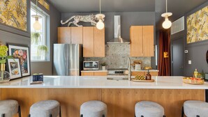 A modern kitchen with a central island, wooden cabinets, stainless steel appliances, and pendant lighting. - The Bloom House & Cosmic Cowgirl by Avantstay Sleeps 17 + 2 Units Gym + Rooftop + Skyline Views (Nashville)
