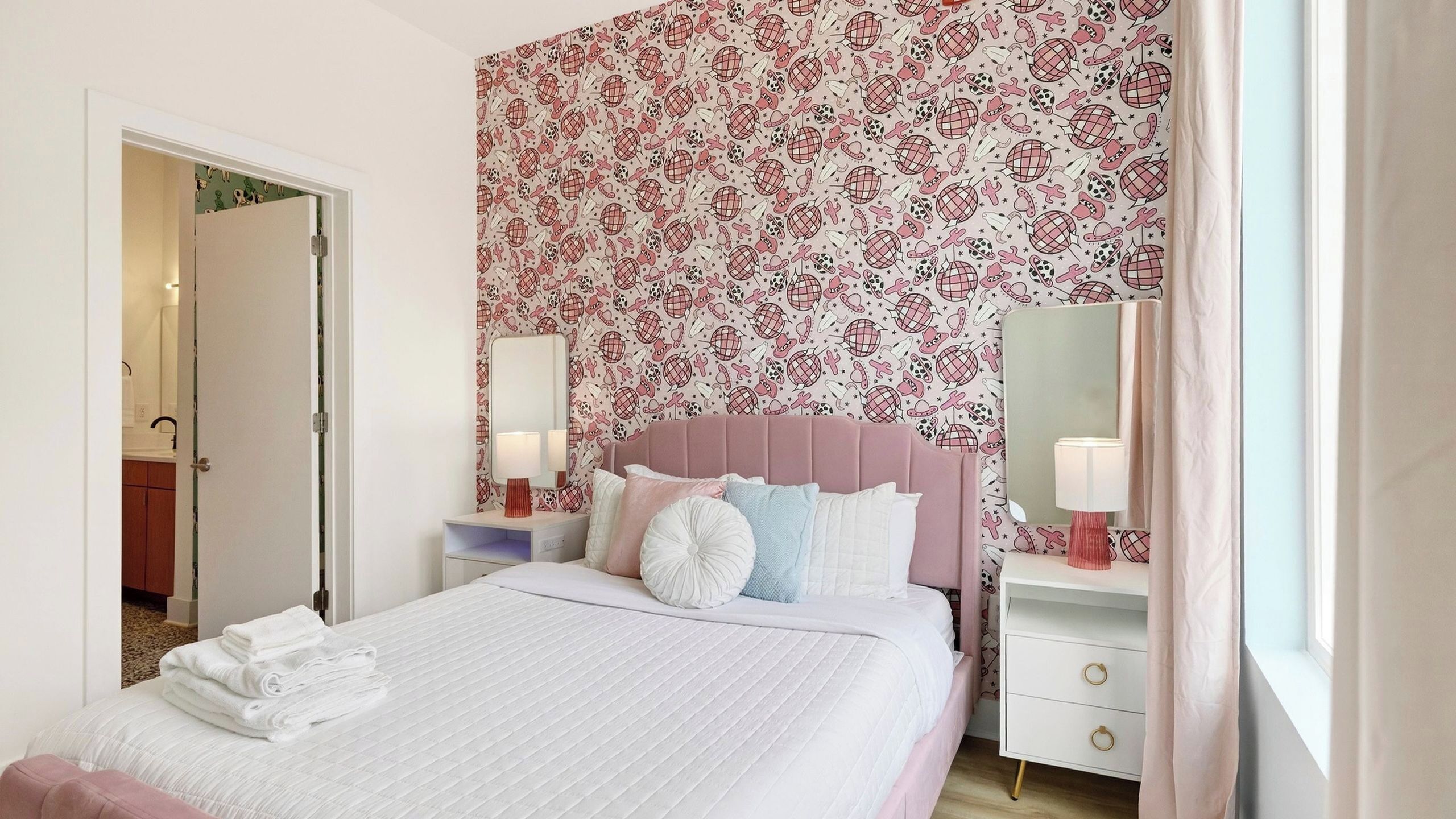 A bedroom with a bed, bedside tables, a mirror, and a floral wallpaper.