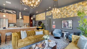 A modern living room with a sofa, armchairs, a coffee table, and a kitchen area with cabinets and a microwave. - The Bloom House & Cosmic Cowgirl by Avantstay Sleeps 17 + 2 Units Gym + Rooftop + Skyline Views (Nashville)