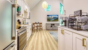 Una cocina moderna con armarios blancos, un comedor con mesa y sillas, una lámpara colgante y una estación de café.