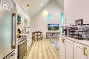 A modern kitchen with white cabinetry, a dining area with a table and chairs, a hanging light fixture, and a coffee station. - Private Hot Tub • Wooded Couples Cabin (Sevierville)