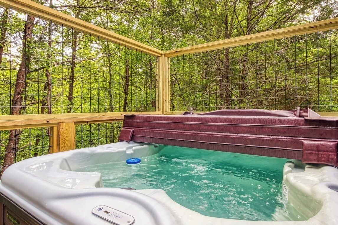Een hottub in een bebost gebied met een houten terras en metalen reling.