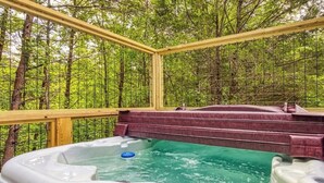 Un jacuzzi en un área boscosa con una terraza de madera y barandilla metálica.