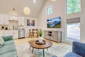 A modern living room with a dining area, kitchen, and large windows. - Private Hot Tub • Wooded Couples Cabin (Sevierville)