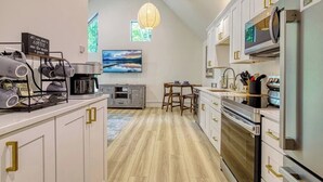 Una cocina moderna con armarios blancos, un comedor con mesa y sillas, un ventanal con vistas y una lámpara colgante.