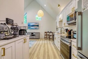 A modern kitchen with white cabinets, a dining area with a table and chairs, a large window with a view, and a hanging light fixture. - Wooded Couples Retreat • Private Hot Tub (Sevierville)