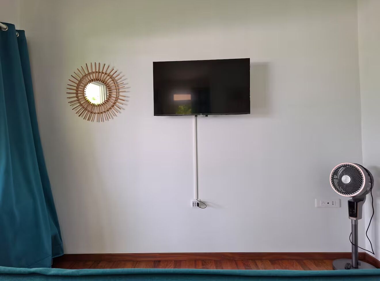 A room with a flat-screen TV mounted on the wall, a standing fan, and a decorative wall light.