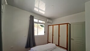 Ein Schlafzimmer mit einem Bett, einem Kleiderschrank, einem Fenster mit Vorhängen und einer Klimaanlage.