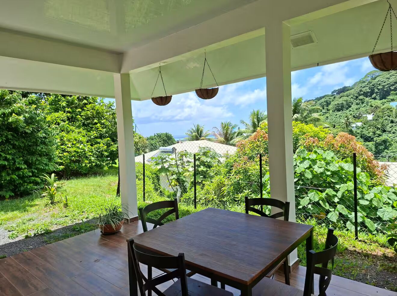 A covered outdoor dining area with a table and chairs, surrounded by lush greenery and a mountainous backdrop.