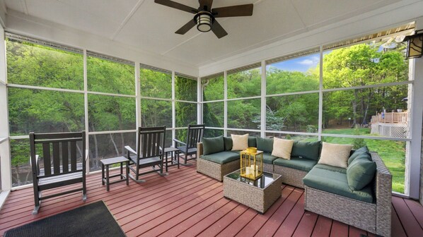 A covered porch with a wooden deck, a sofa with cushions, two chairs, and a ceiling fan. - Belle Pines Hideaway by Avantstay Lakefront + Hot Tub + Fire Pit + Game Room Near Charlotte (Sherrills Ford)