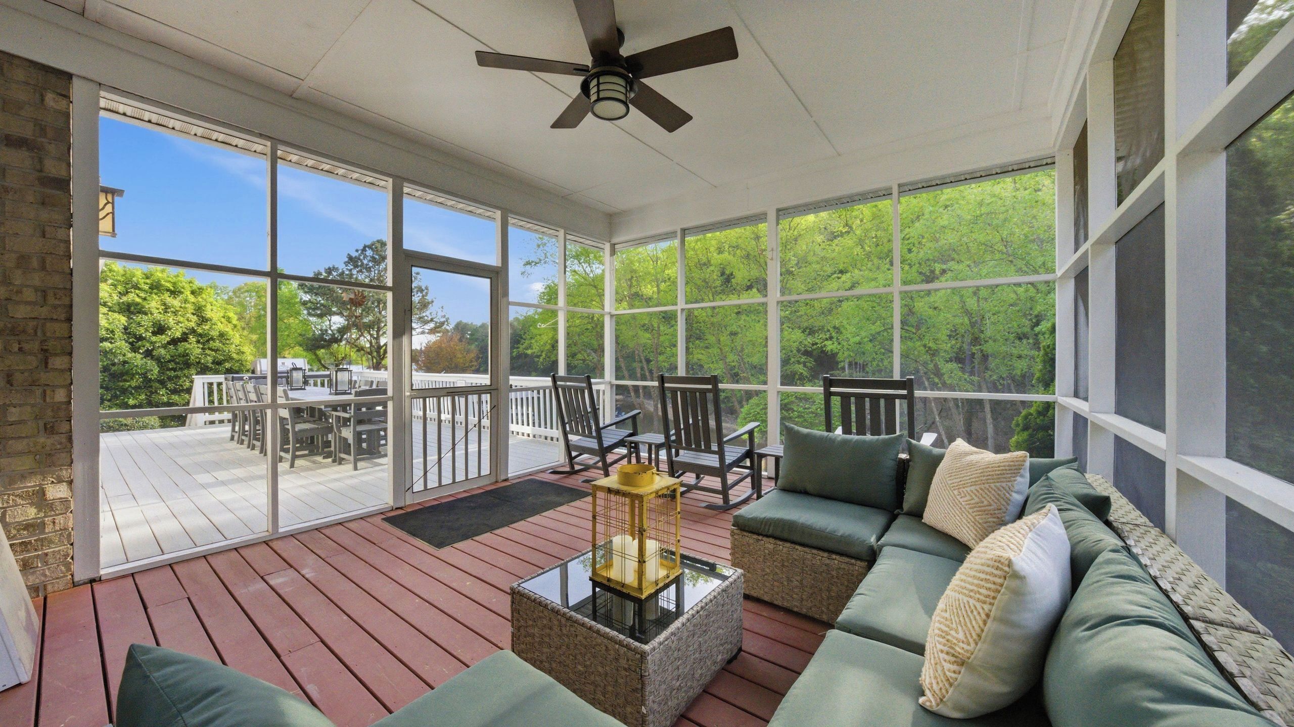 A screened porch with a ceiling fan, outdoor furniture, and a view of the surrounding greenery.